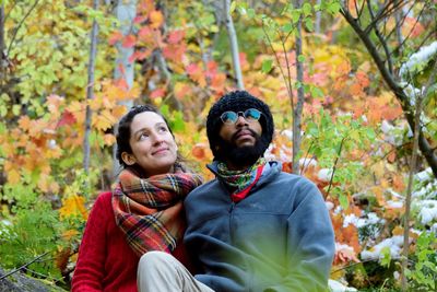 Young couple looking up while sitting against plants