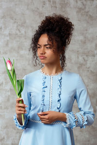 Sad young woman holding flower while standing against wall