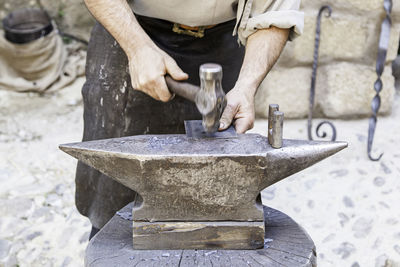 Midsection of man hammering metal at workshop