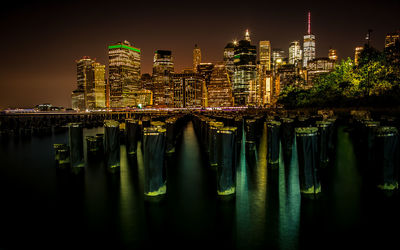Illuminated modern building by river against sky at night