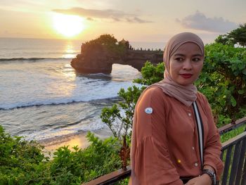 Portrait of young woman standing against sea during sunset