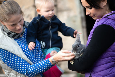 Mother with son looking at rabbit being held by woman in park