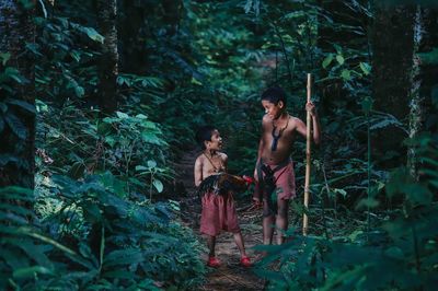 Boys with rooster standing amidst trees