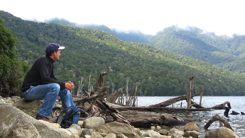 Side view of mature man sitting on rock by lake and mountains