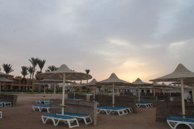 Lounge chairs by swimming pool at beach against sky during sunset