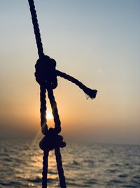 Close-up of silhouette rope on beach against sky during sunset