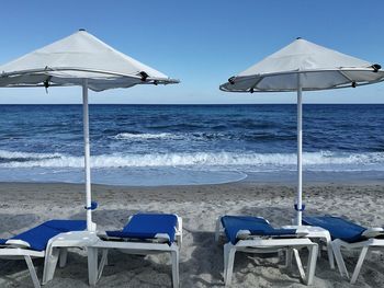 Deck chairs on beach against clear blue sky