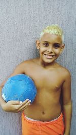 Portrait of shirtless boy holding ball against wall