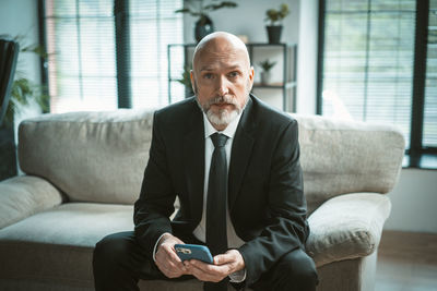 Portrait of young man using phone while sitting on sofa at home