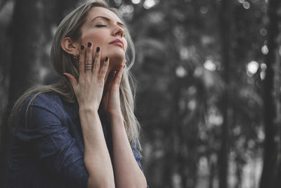 Close-up of young woman with hand on tree