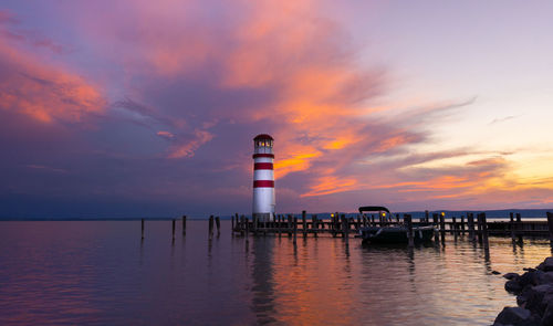 Lighthouse by sea against sky during sunset