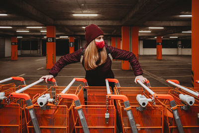 Woman with mask holding row of orange shopping carts in garage