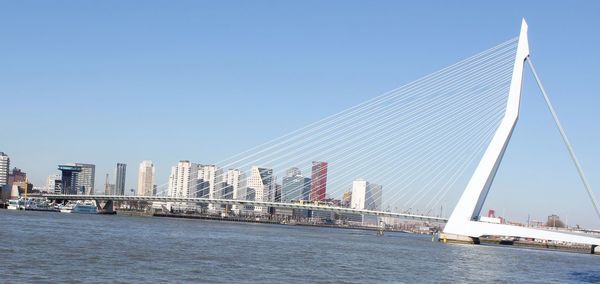Suspension bridge over river and buildings against clear sky