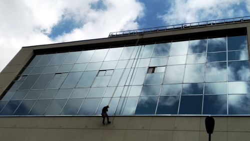 Low angle view of people walking on modern building against sky