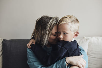 Mother embracing son while sitting on sofa at home
