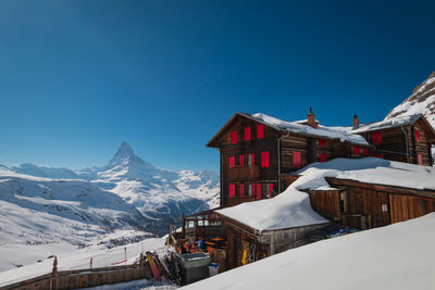 Houses by snow covered mountains against clear blue sky