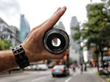 Cropped image of hand holding lens on city street