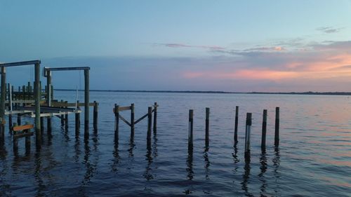 Wooden posts in sea against sky during sunset