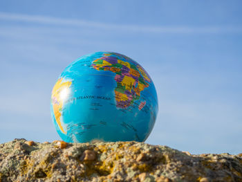 Low angle view of globe on rock against blue sky