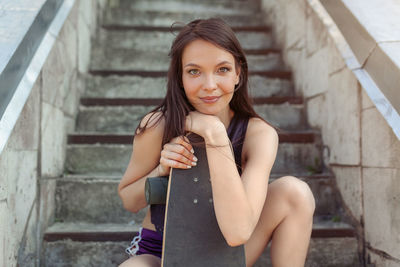 Portrait of smiling young woman with skateboard sitting by steps