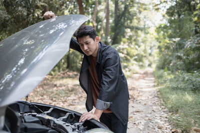 Young man standing on car in forest