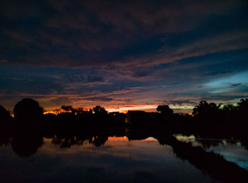 Silhouette trees by lake against sky during sunset