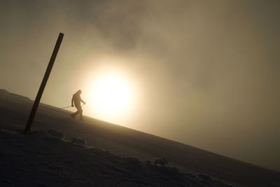 Silhouette person on land against sky during sunset