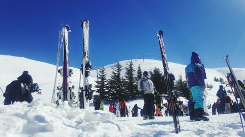 Low angle view of people on snow covered mountain against blue sky