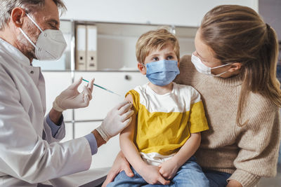 Boy being vaccinated by doctor while on lap of mother