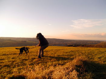 Man with dog on landscape against sky during sunset