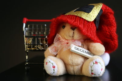 Close-up of stuffed toy wearing knit hat with shopping cart on table against black background