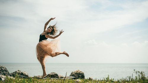 Woman dancing at beach against sky