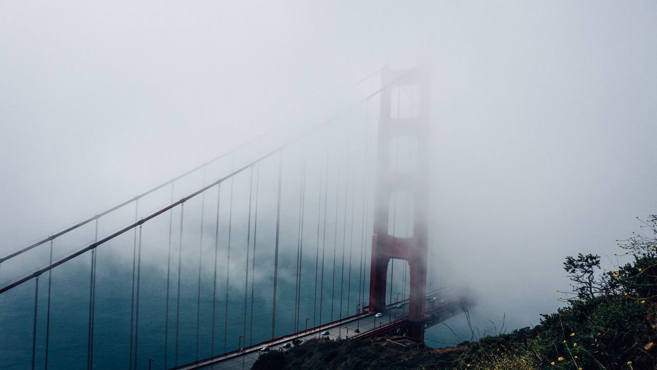 architecture, built structure, low angle view, bridge - man made structure, connection, sky, suspension bridge, modern, engineering, fog, building exterior, city, skyscraper, travel destinations, tall - high, famous place, travel, weather, day