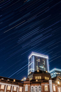 Low angle view of illuminated building against star trails at night