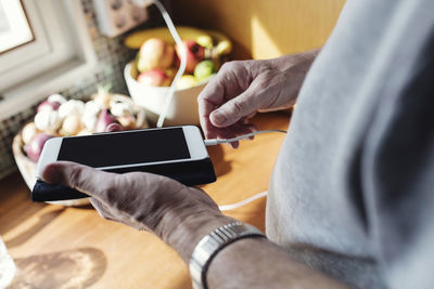 Cropped image of senior man connecting cable to mobile phone at kitchen counter