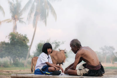 Friends sitting on palm tree against sky