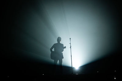 Silhouette man standing against illuminated lamp at night