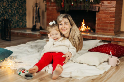 Mom and daughter are playing with christmas garlands on the floor by the fireplace