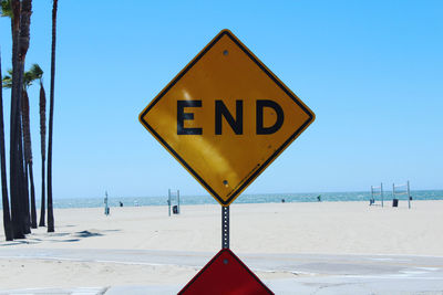 Road sign on beach against clear blue sky
