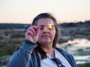 Woman holding sparkler against sky during sunset