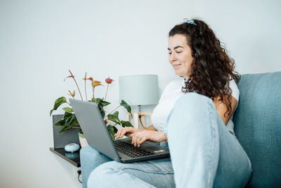 Young woman using laptop while sitting on sofa at home