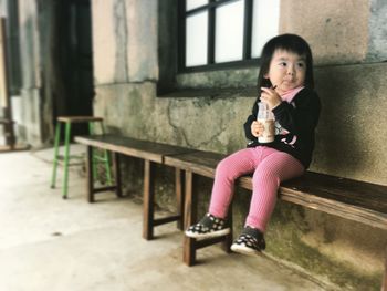 Full length of girl sitting with milk bottle on table