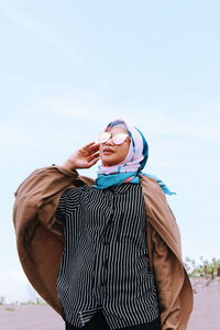 Young woman wearing sunglasses standing against sky