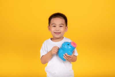 Smiling boy holding yellow camera against orange background