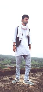 Young man looking away while standing on land against sky