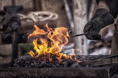 Cropped hand holding metal in bonfire at workshop