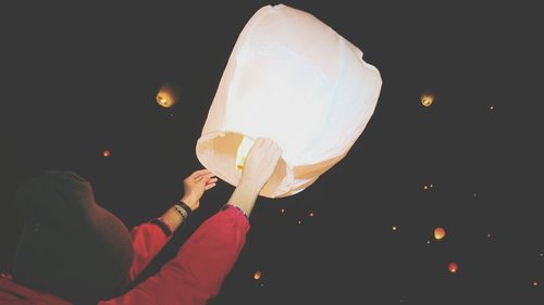 Low angle view of hand holding balloons against sky at night