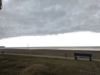 Bench on field by sea against sky