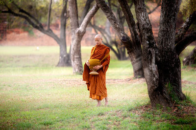 Full length of monk wearing traditional clothing standing in forest