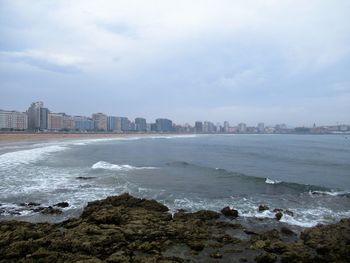 Scenic view of sea by cityscape against sky